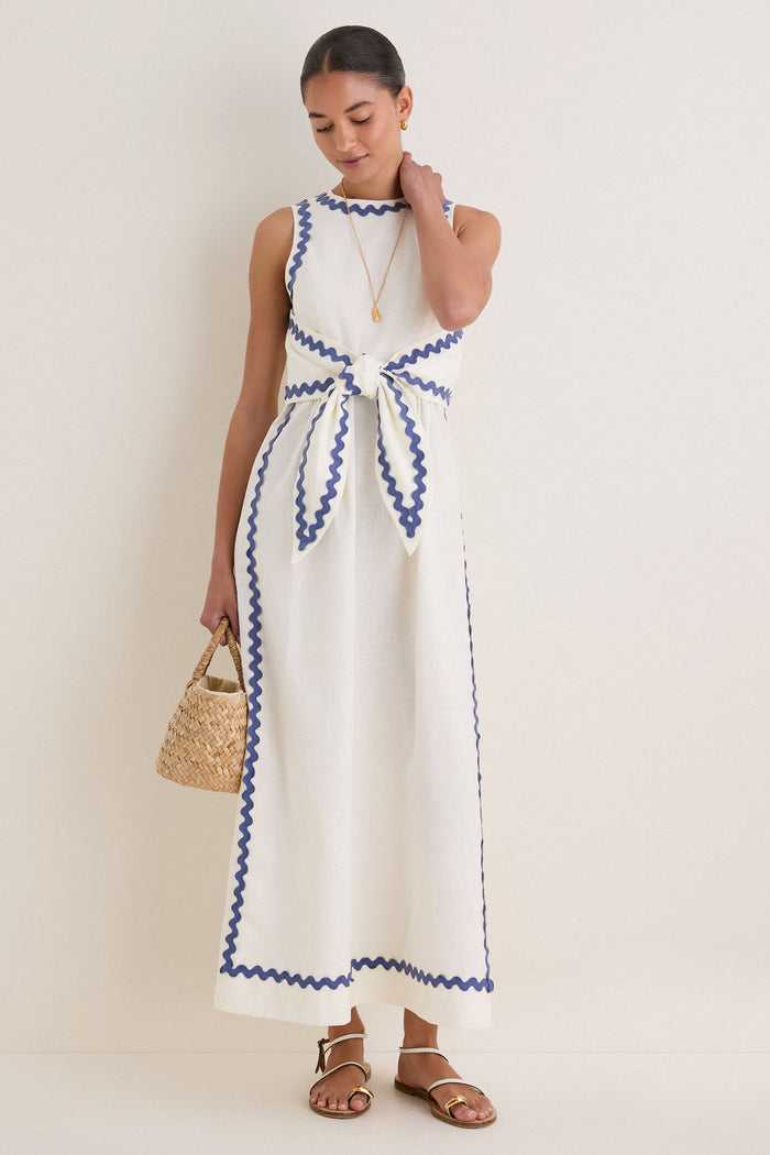 Woman in White Ric Rac Tie-Front Brocks Dress, a classic and effortless ankle-length piece, accessorized with a woven straw bag, embodying fun, high-end style.