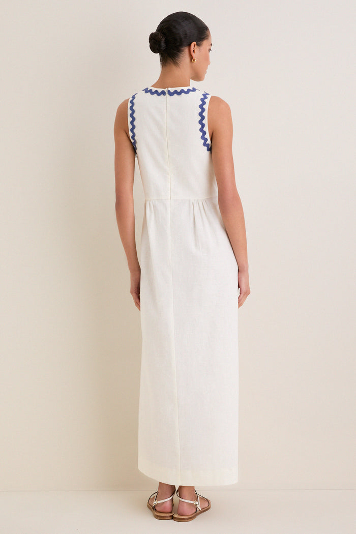 Woman in a classic, sleeveless White Ric Rac Tie-Front Brocks Dress with wavy blue trim, embodying an effortless and high-end style, paired with fun, simple white sandals.