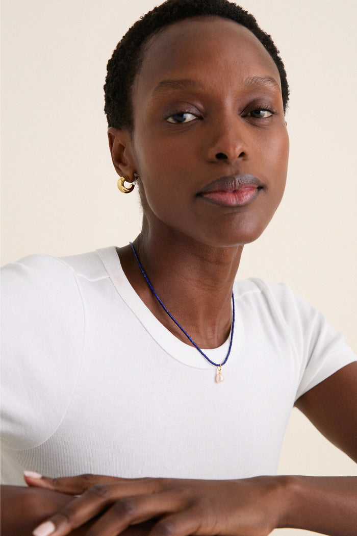 Woman wearing the classic Lapis Lazuli Teeny Gemstone Necklace with Cloud Pearl Charm, embodying effortless style with its fun, high-end design.