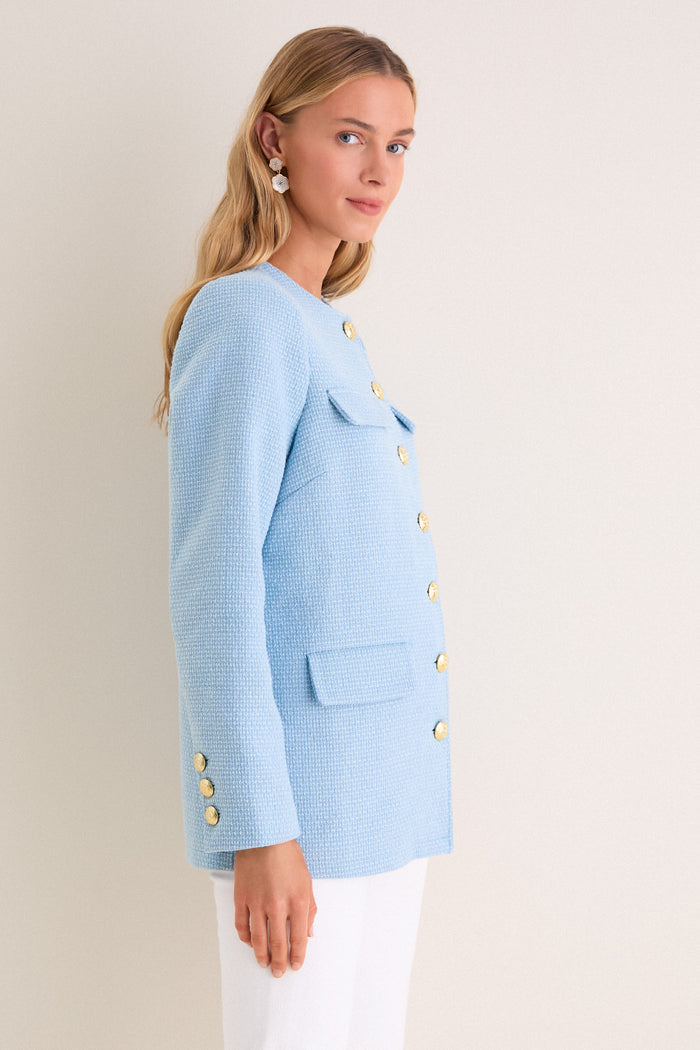 Woman wearing classic Light Blue Tweed Jennings Jacket with gold buttons and flap pockets, paired with white pants; an effortless, high-end look.