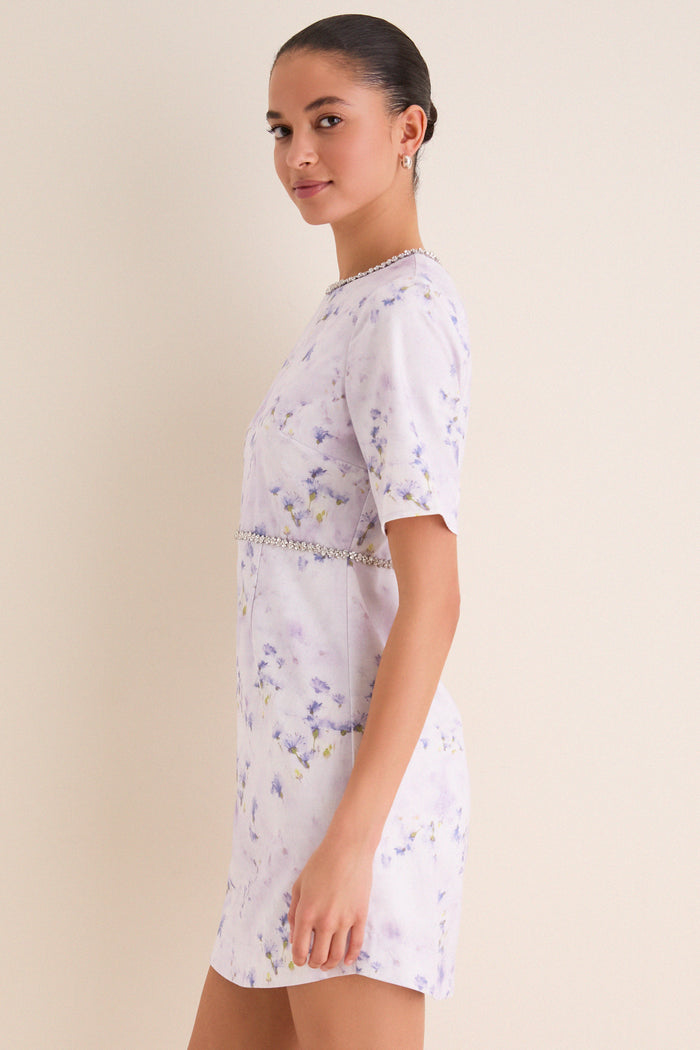 Young woman in profile wearing the Lilac Floral Crystal Embellished Floria Mini Dress, showcasing its classic, effortless design with fun, high-end beaded waist detail.