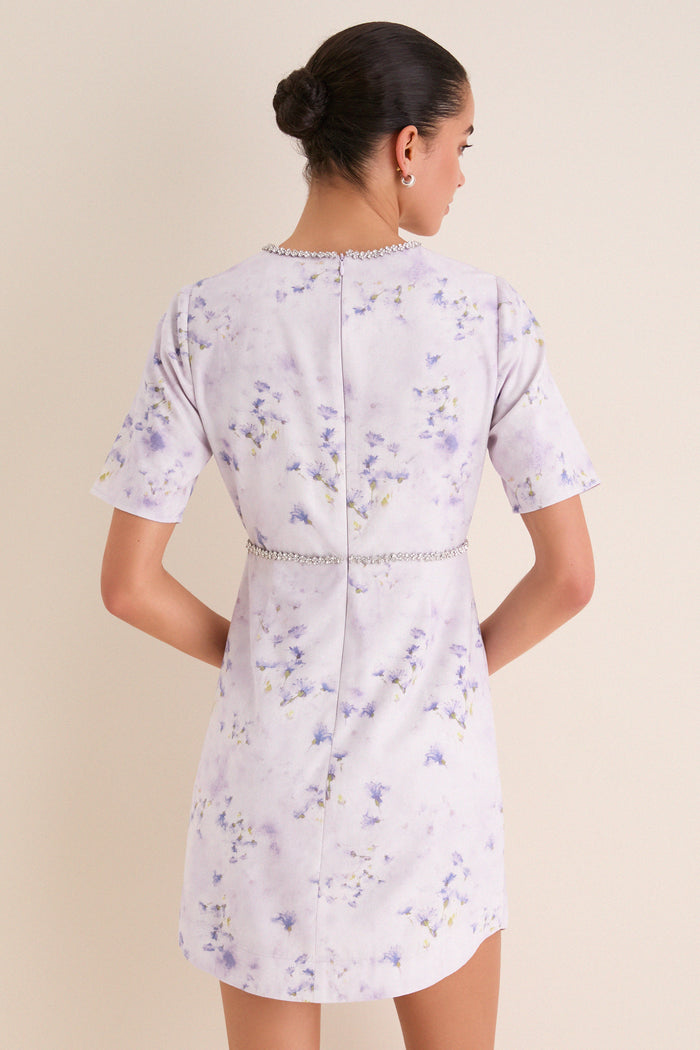 Back view of a woman in the Lilac Floral Crystal Embellished Floria Mini Dress, showcasing its classic, effortless design with a fun, high-end floral pattern.