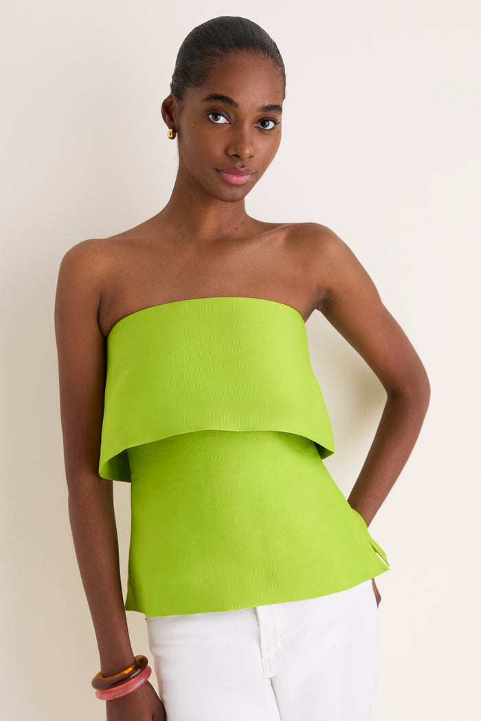 Young Black woman wearing a classic, lime Felix Satin Strapless Top with fold-over neckline, styled effortlessly with white pants and gold accessories, embodying high-end, fun fashion.