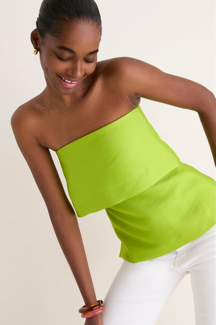Young woman in a classic, high-end Lime Felix Satin Strapless Top with fold-over neckline, exemplifying effortless style and fun elegance, paired with chic white pants.