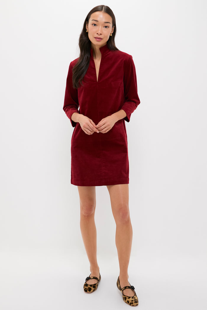 A woman faces forward against a plain white background, wearing a long-sleeved, knee-length red Clifton Dress by Tuckernuck and leopard print flats.