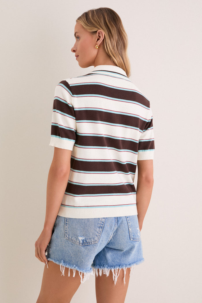 Woman in a classic Mint Chocolate Stripe Reid Polo Cardigan with bold stripes, embodying effortless and fun style, paired with high-end frayed denim shorts.