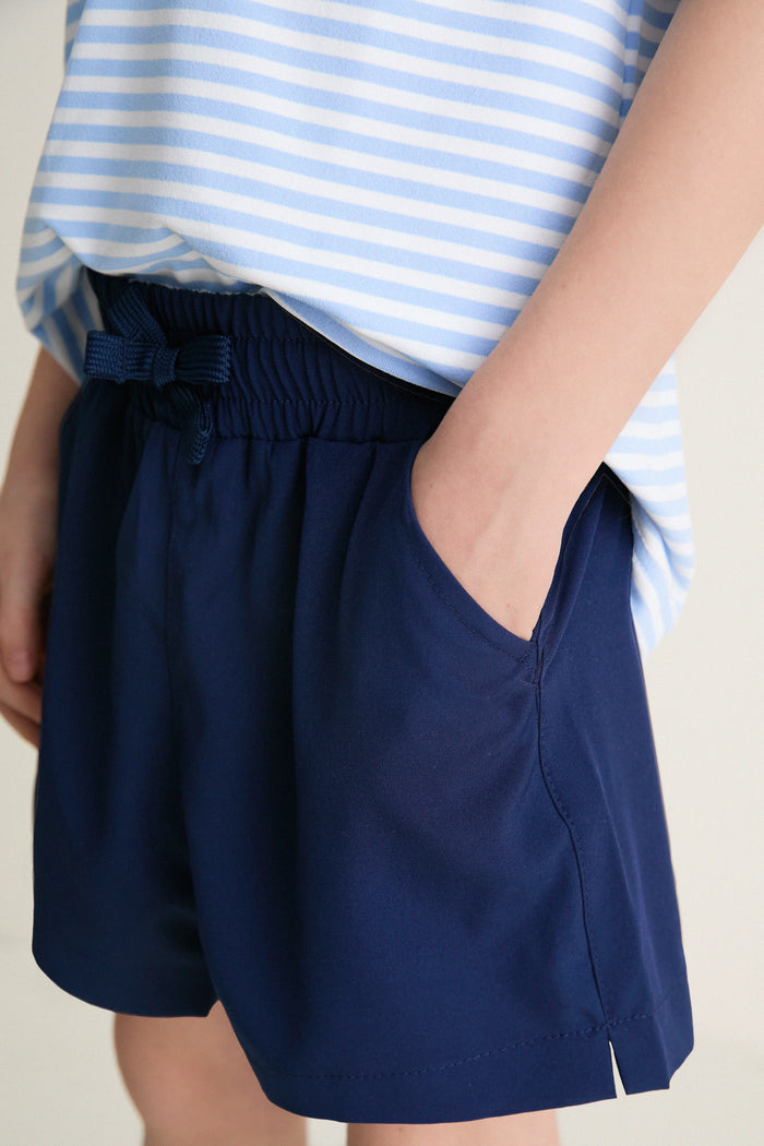 Classic Nautical Navy Le Club Short, offering effortless style and fun with its high-end, lightweight design, shown with a tucked striped top and casual pocketed stance.