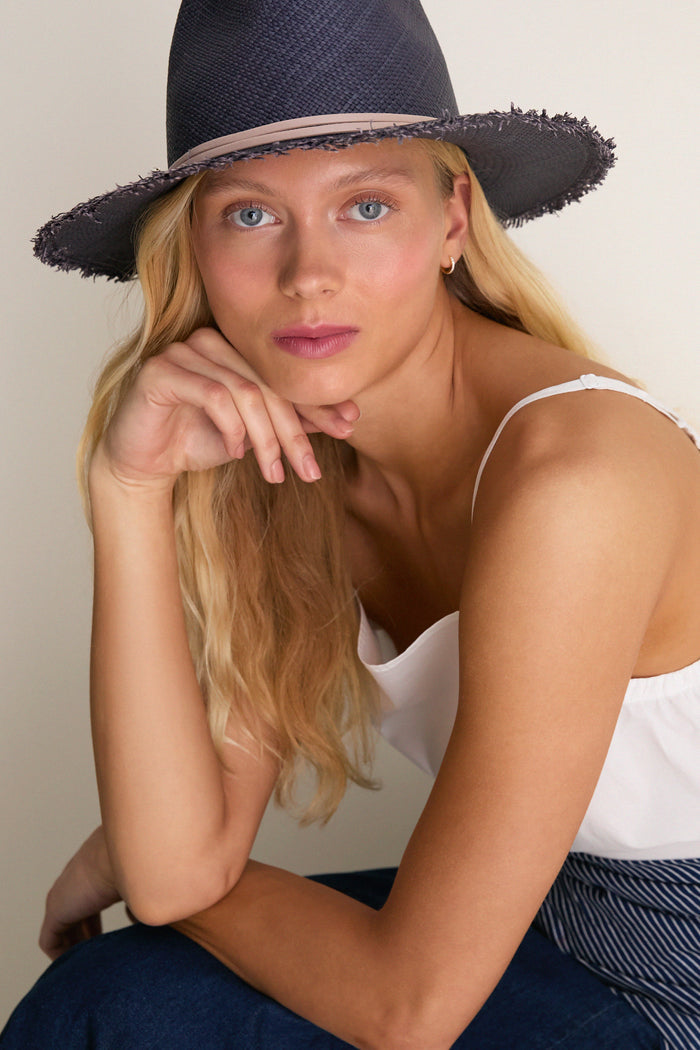 Young woman in a classic, effortless pose wearing the Navy and Tan Fringed Pammy Panama Continental Hat, showcasing its playful fringe brim for a high-end, sun-ready style.