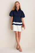 Woman wearing the classic Navy and White Stripe Mini Delaney Dress with a fitted bodice and puffed sleeves, holding a woven clutch, exuding an effortless, high-end style.