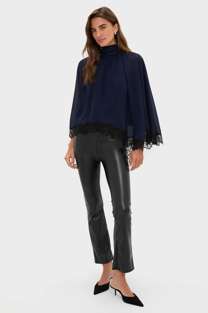 Model wearing the classic Navy Cape Chiffon Ashfield Top with a high mock neck, cape sleeves, and bow detail, paired with black leather pants and mule heels, exuding effortless high-end style.