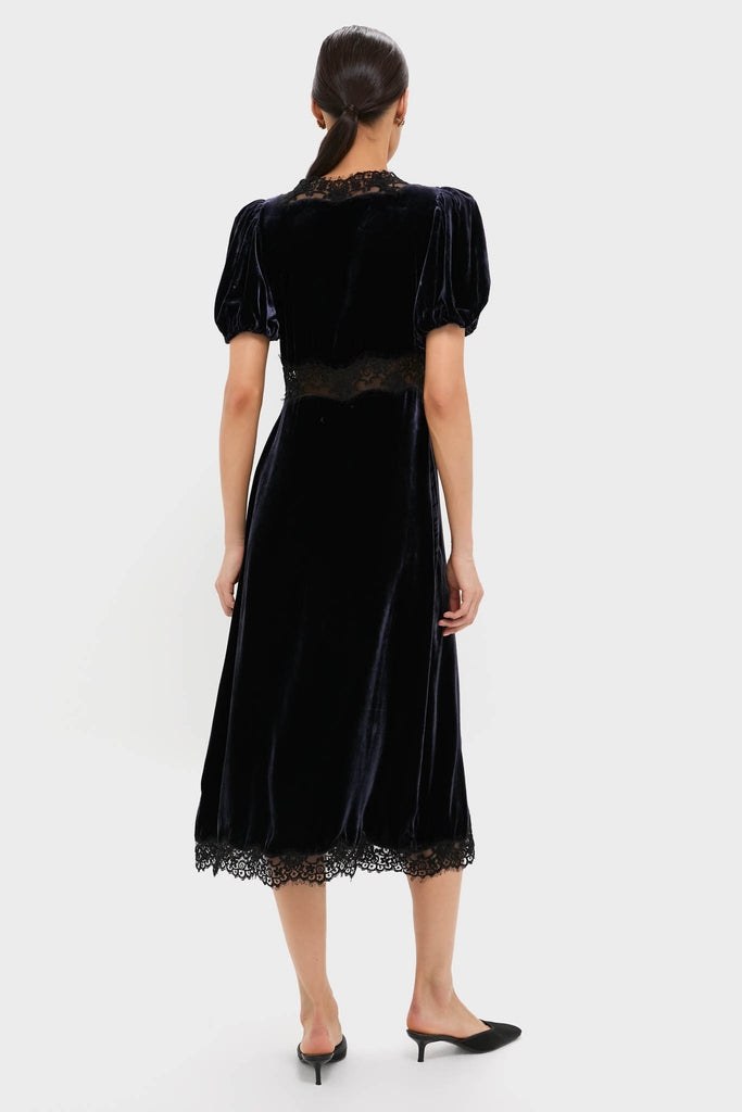 Model wearing Navy Clarice Velvet Puff Sleeve Midi Dress, featuring a classic, effortless silhouette with puffed sleeves, lace insets, and scalloped hem; styled with black mules.