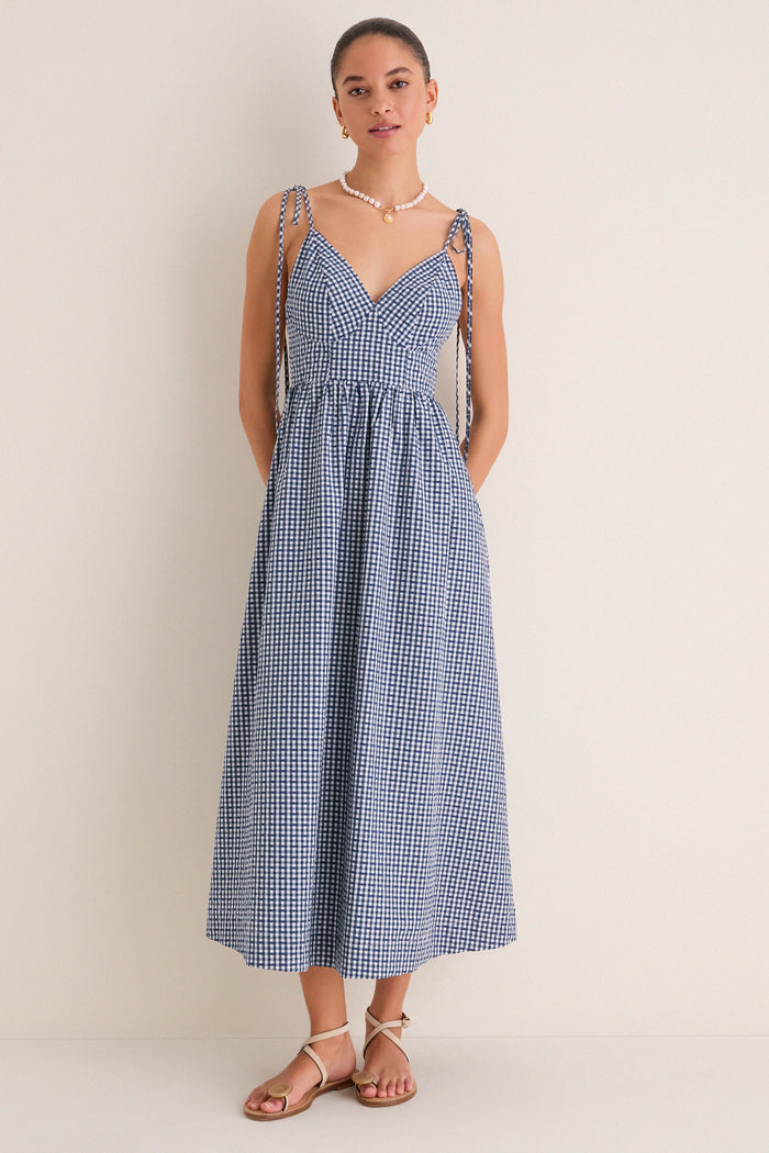 Navy Gingham Sloan Maxi Dress: Effortless and classic, this sleeveless sundress features a V-neck, tie straps, and smocked back, styled with pearl necklace and tan sandals.