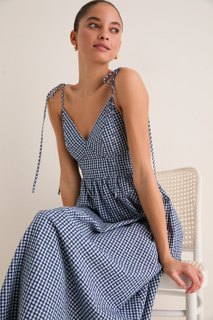 Navy Gingham Sloan Maxi Dress: A young woman in a classic, effortless gingham maxi dress with tie straps and a V-neckline, exuding high-end, fun sophistication.