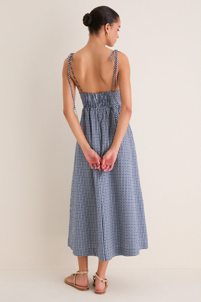 Back view of a woman in the classic Navy Gingham Sloan Maxi Dress with tie straps, showcasing its effortless and fun smocked back and elegant silhouette.