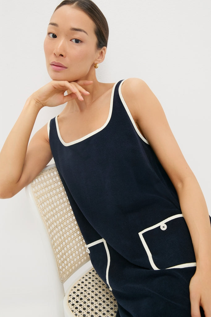 Young woman in a classic, high-end Navy Mini Terrycloth Button Tank Dress, exuding effortless style and fun, seated elegantly on a cane-back chair.