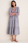 Woman in Navy Prism Embroidered Gingham Long Sleeve Salty Paloma Caftan, showcasing its classic, effortless design with tiered skirt and red embroidery, paired with brown leather sandals.