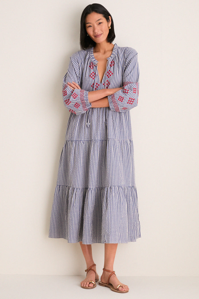 Woman in Navy Prism Embroidered Gingham Long Sleeve Salty Paloma Caftan, showcasing its classic, effortless design with tiered skirt and red embroidery, paired with brown leather sandals.