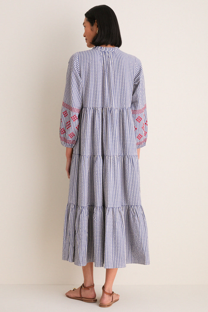 Woman in a classic, effortless Navy Prism Embroidered Gingham Long Sleeve Salty Paloma Caftan with tiered skirt and red embroidered balloon sleeves, embodying high-end, fun style.
