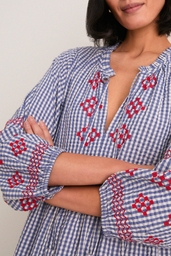 Woman in a classic, effortless Navy Prism Embroidered Gingham Long Sleeve Salty Paloma Caftan with ruffled neckline and embroidered details, embodying fun, high-end bohemian style.