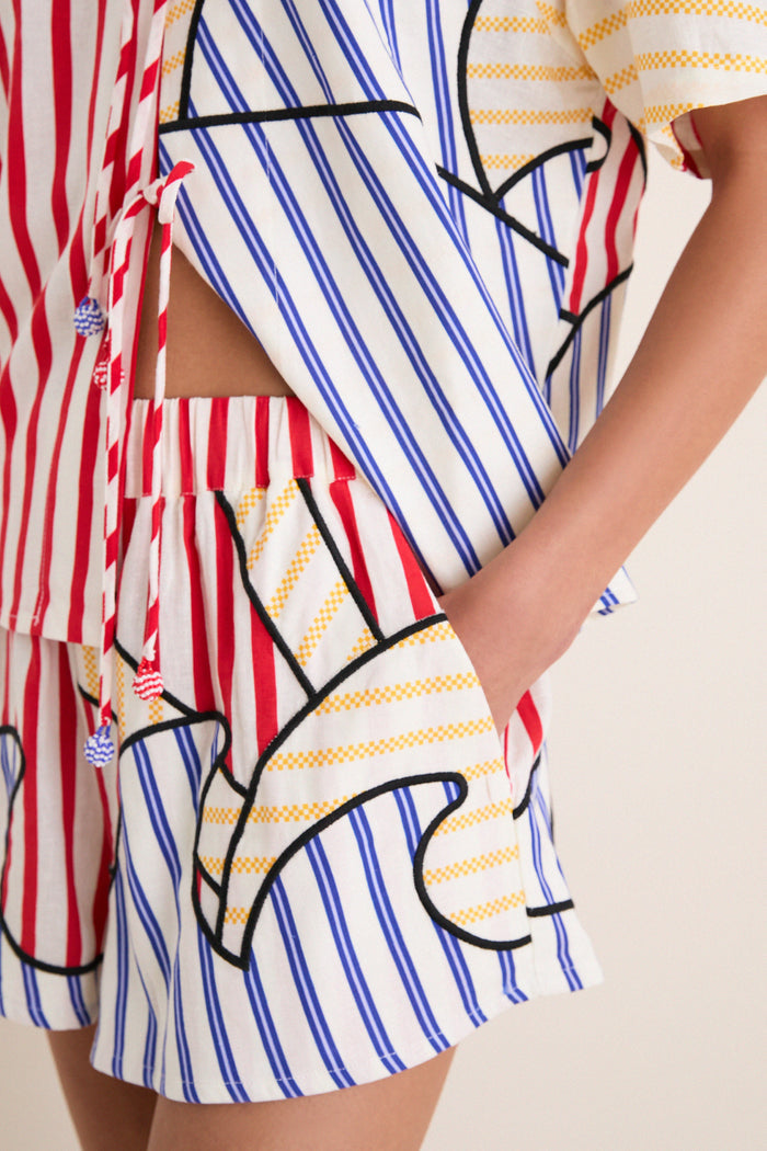 Model wearing Navy Stripes Off-White Shorts in a playful, multi-colored stripe pattern with an elastic waistband and side seam pockets for a classic, effortless style.