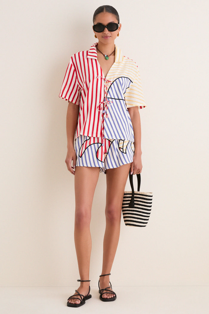 Model in the Navy Stripes Off-White Tie Front Blouse with matching shorts, exuding an effortless, fun vibe. A classic, high-end summer look completed with black sandals and a woven tote.
