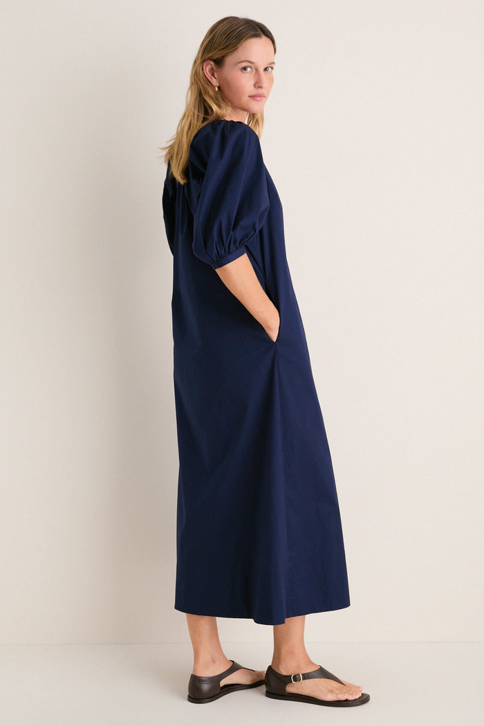 Woman in a classic, effortless Navy Vincent Dress with balloon sleeves and side pockets, embodying high-end simplicity and fun style with dark brown sandals.