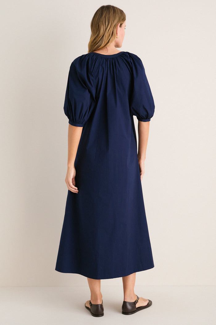 Back view of a woman in the classic Navy Vincent Dress with puff sleeves and button-down front, styled with simple sandals for an effortless, high-end look.
