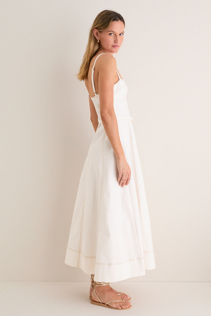 Model in profile wearing the Off White Fiona Dress, a classic, ankle-length piece with spaghetti straps and a flared skirt, paired with effortless gold sandals.