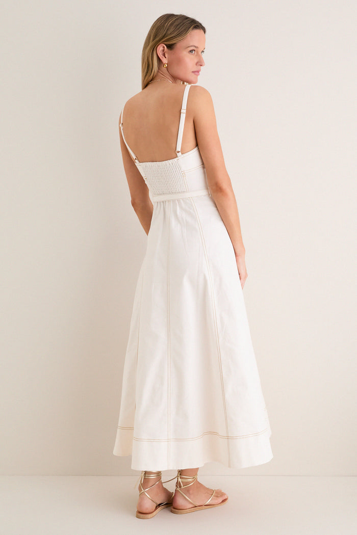 Woman models the classic Off White Fiona Dress, featuring an effortless fitted smocked bodice, A-line skirt, adjustable straps; paired with fun, high-end gold-tone sandals and hoop earrings.
