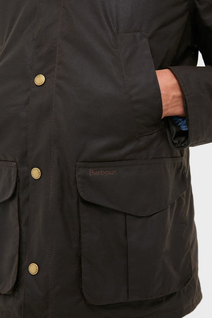 Barbour Olive Hereford Wax Jacket close-up, showcasing classic, effortless style with hand-warmer pockets, brass snap-buttons, and embroidered logo, embodying high-end, fun sophistication.