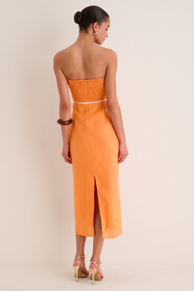 Woman in Orange Linen Clementine Maxi Dress, featuring a classic strapless, asymmetrical neckline and smocked back, accessorized with gold hoops and sandals, radiating effortless high-end style.