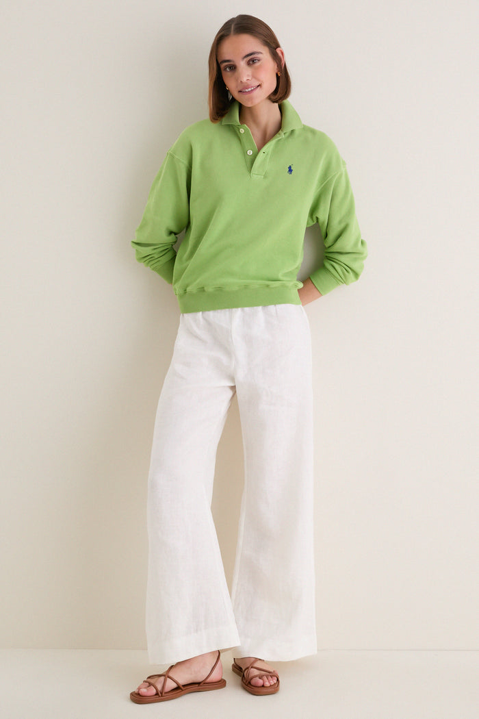 Young woman in a classic, high-end Parakeet Green Island Fleece Knit Polo and white linen-blend trousers, exuding effortless, fun style.