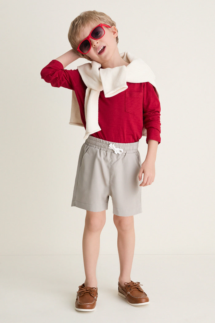 Young boy in Patagonian Putty Le Club Short, styled with a red shirt and cream sweater, embodies classic, effortless style with fun, high-end comfort and versatility.