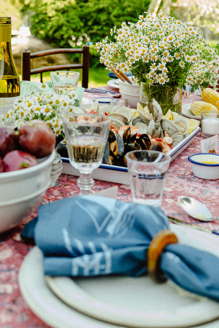 Close up of a summer table setting with a red tablecloth, a blue sailboat napkin, and blue silverware.