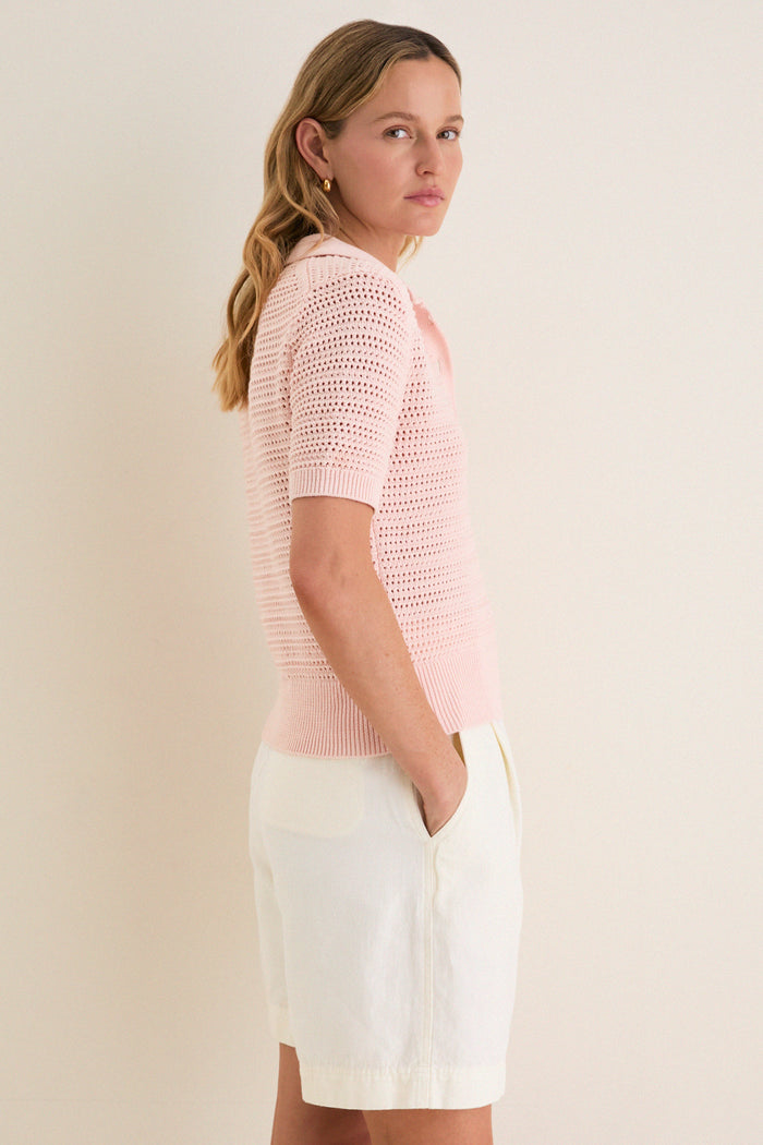Young woman in profile wearing the classic Pink Crochet Cotton Asher Polo, showcasing its effortless, high-end style paired with high-waisted shorts, embodying fun elegance.