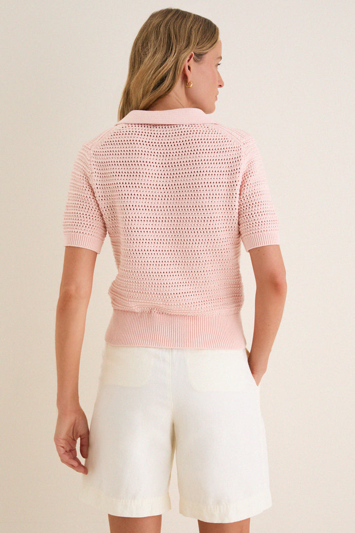 Back view of Pink Crochet Cotton Asher Polo, a classic, effortless knit with short sleeves and a three-button placket, tucked into high-waisted white shorts.