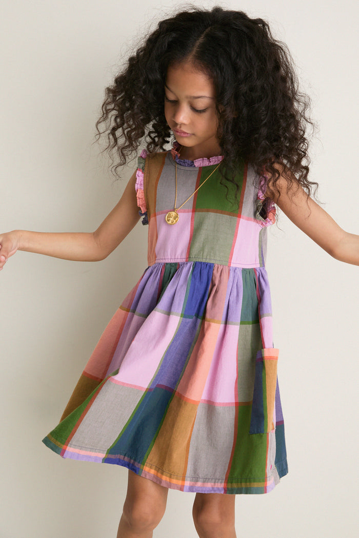 Young girl in classic Plaid Madras Alyssa Dress with patch pockets, ruffle detailing, and silver buttons, embodying effortless, fun style for high-end comfort.