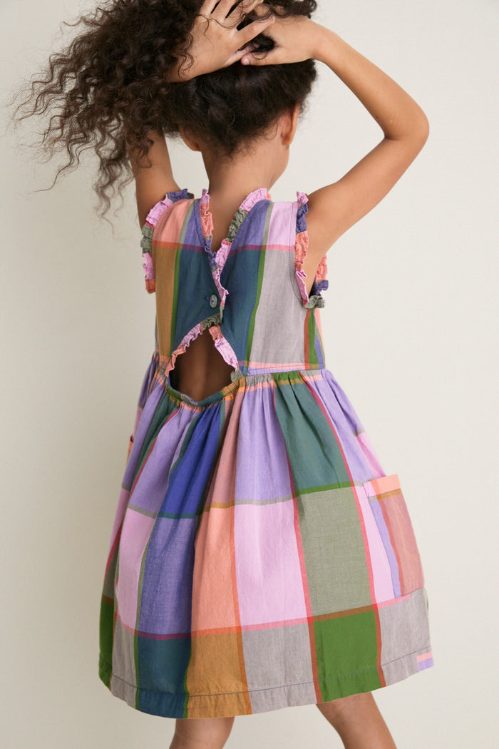 Young child in a classic, sleeveless Plaid Madras Alyssa Dress with ruffle trims, keyhole back, and raised arms, embodying effortless, fun style.