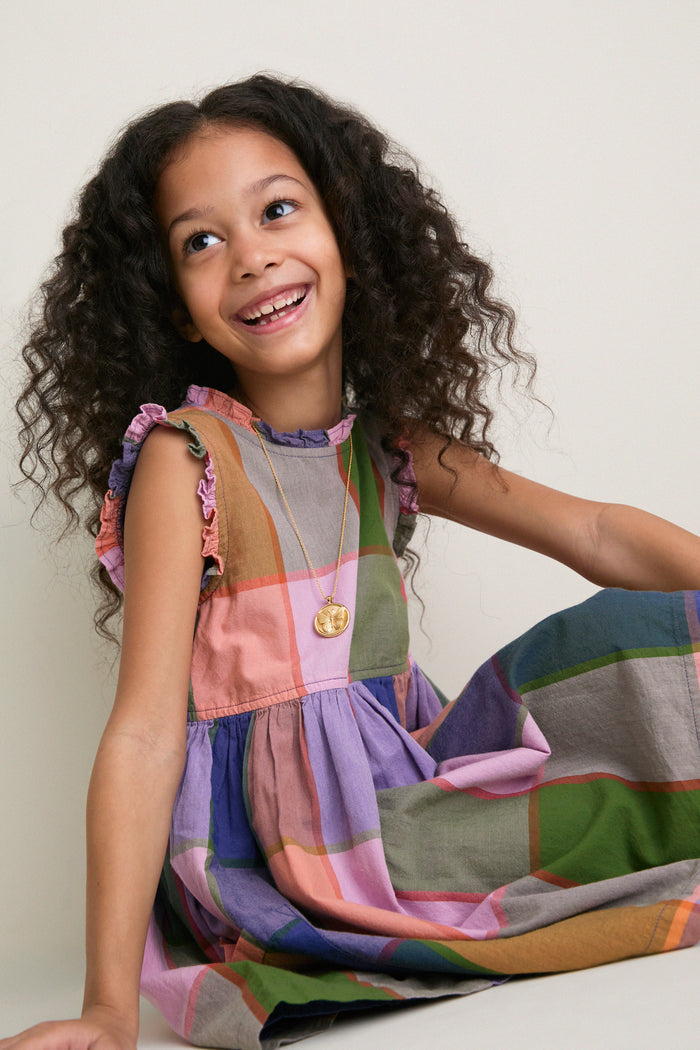 Young girl in Plaid Madras Alyssa Dress, featuring playful ruffles and silver buttons, exudes effortless, fun style, embodying classic, high-end charm.
