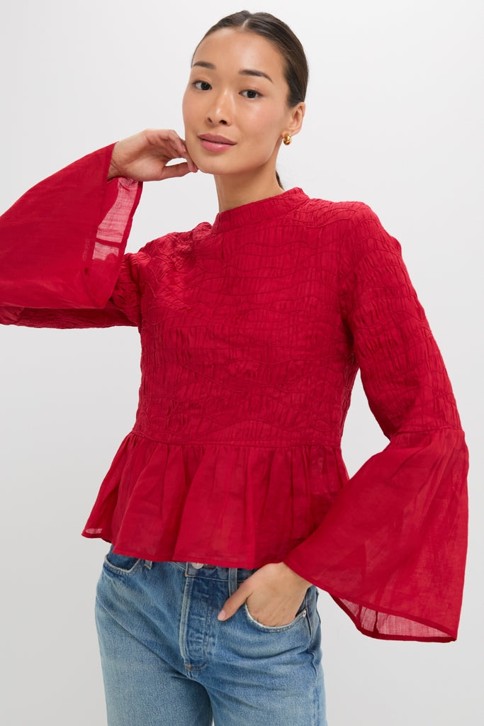 Woman wearing classic Red Imogen Solid Long Sleeve Top with bell sleeves and peplum hem, paired with light jeans. An effortless, high-end style for fun, confident looks.