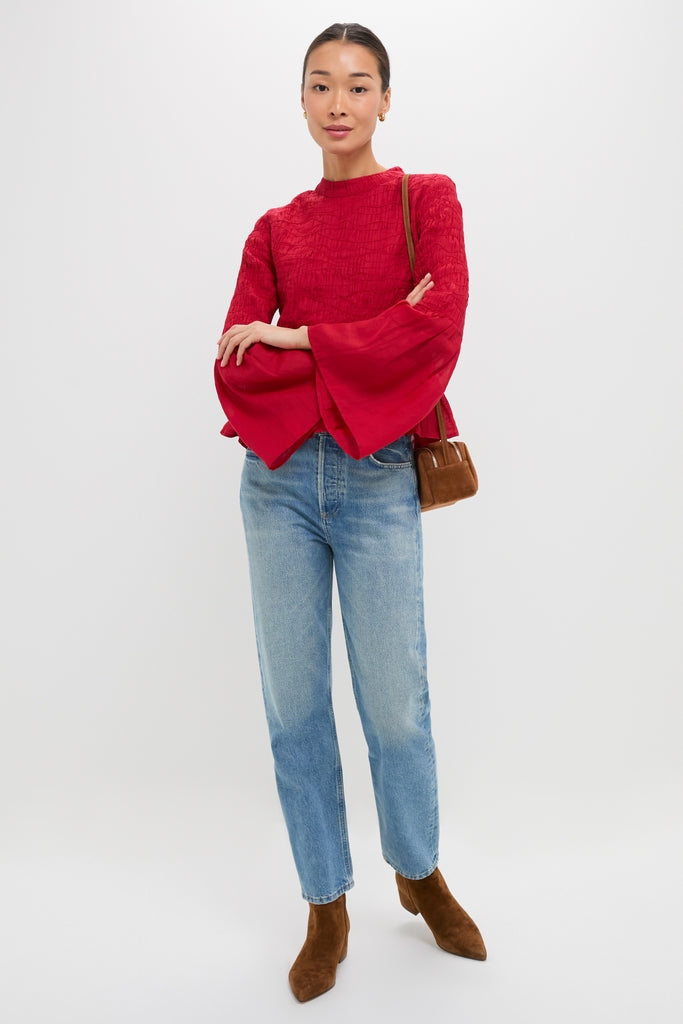 Woman in a classic Red Imogen Solid Long Sleeve Top with bell sleeves and peplum hem, paired with jeans and boots, exuding an effortless, high-end style.