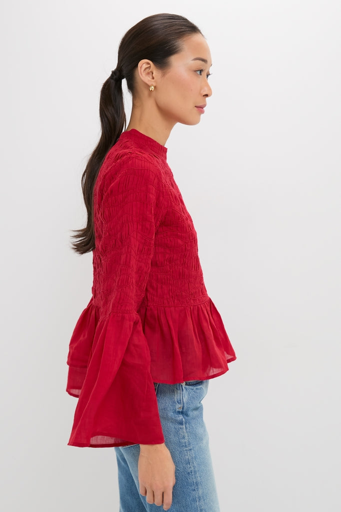 Young woman in profile wearing the classic Red Imogen Solid Long Sleeve Top with bell sleeves and peplum hem, paired effortlessly with light-wash jeans, exuding a fun, high-end vibe.