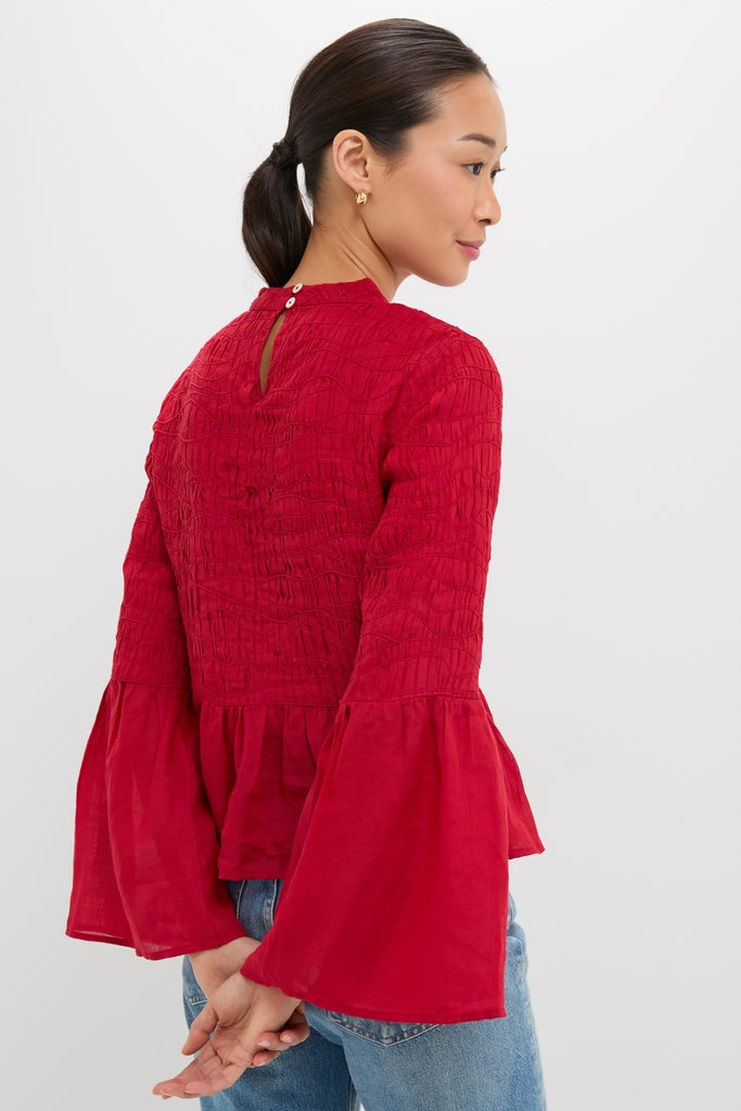 Woman in a classic, high-end Red Imogen Solid Long Sleeve Top with bell sleeves, peplum hem, and keyhole closure, styled effortlessly with jeans.