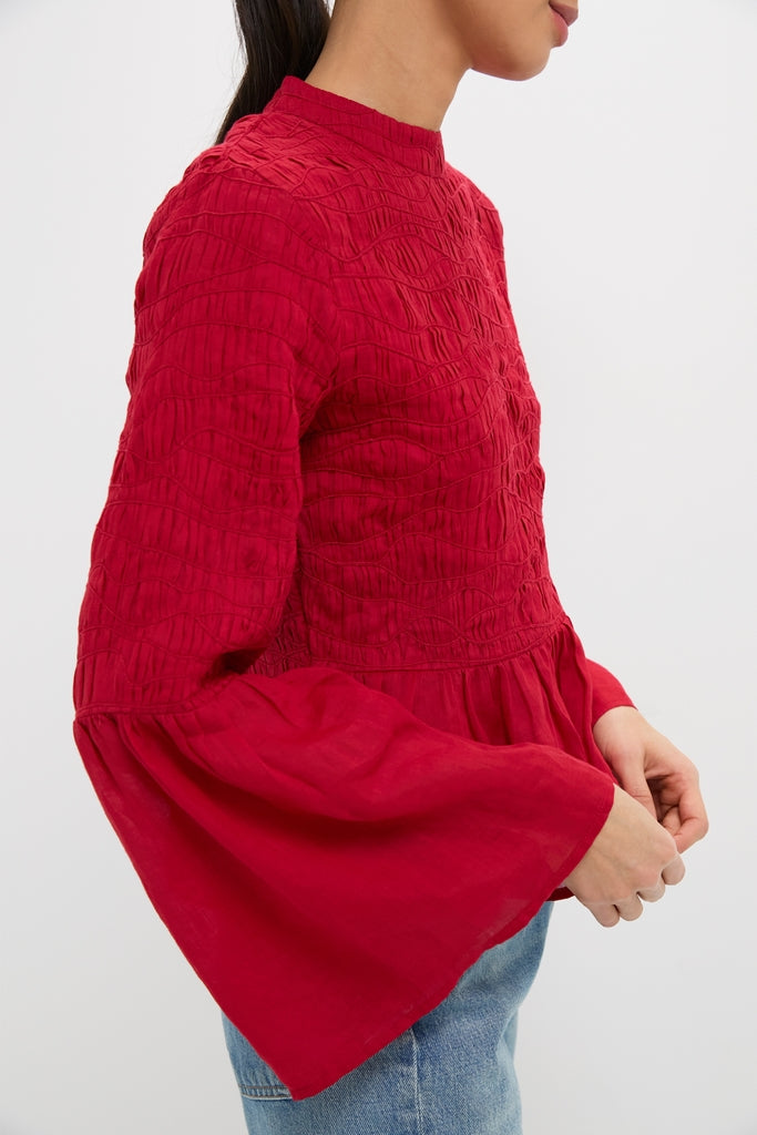 Woman in a classic, high-neck Red Imogen Solid Long Sleeve Top with pintuck details and dramatic bell sleeves, paired effortlessly with light-wash jeans for a high-end, fun look.
