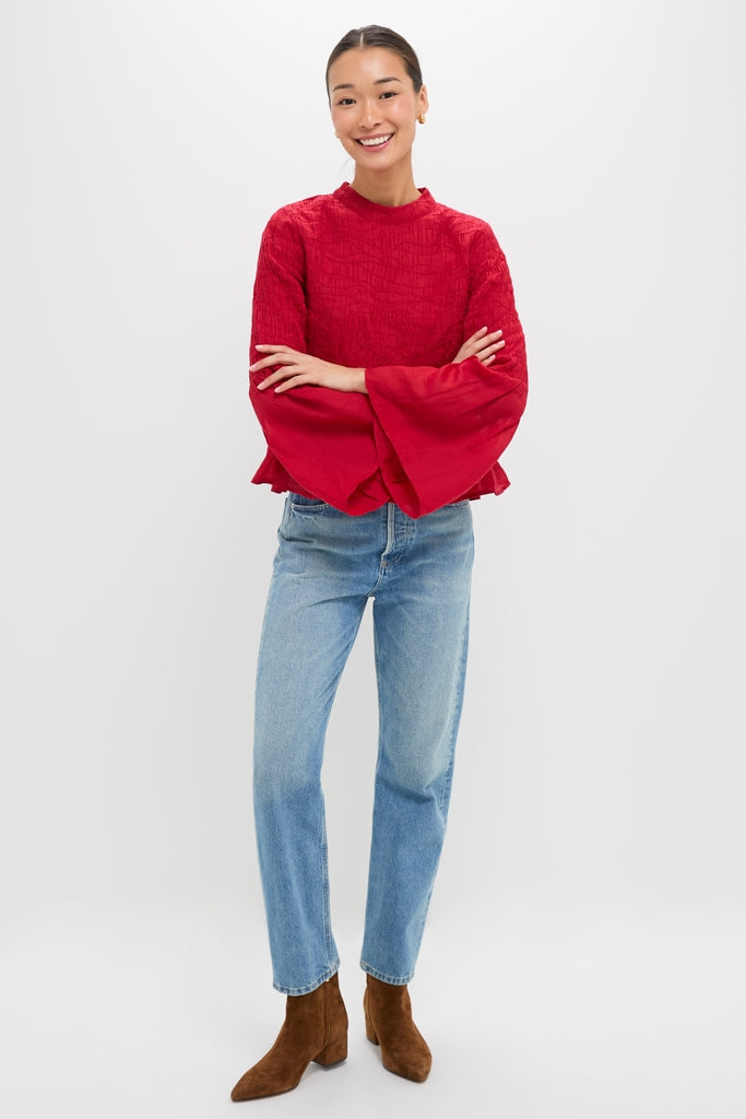 Young woman models the Red Imogen Solid Long Sleeve Top with pintuck detailing, bell sleeves, and peplum hem, paired with jeans and ankle boots for an effortless, high-end look.