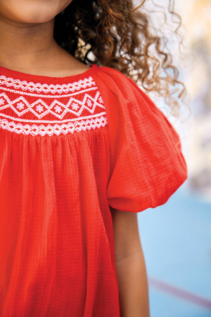 Child wearing the Red Nala Dress with white embroidered neckline and puff sleeves, embodying classic and effortless high-end style, perfect for a fun, chic look.