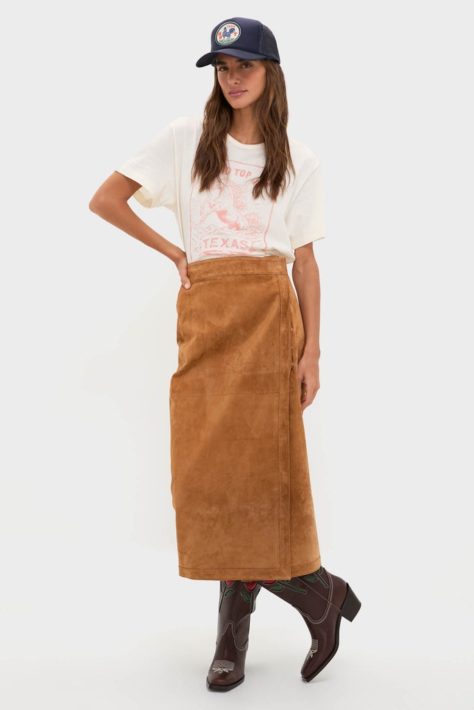 Young woman models a classic, effortless Western look featuring a fun, high-end Round Top Trucker Hat, paired with a graphic tee, suede skirt, and cowboy boots.