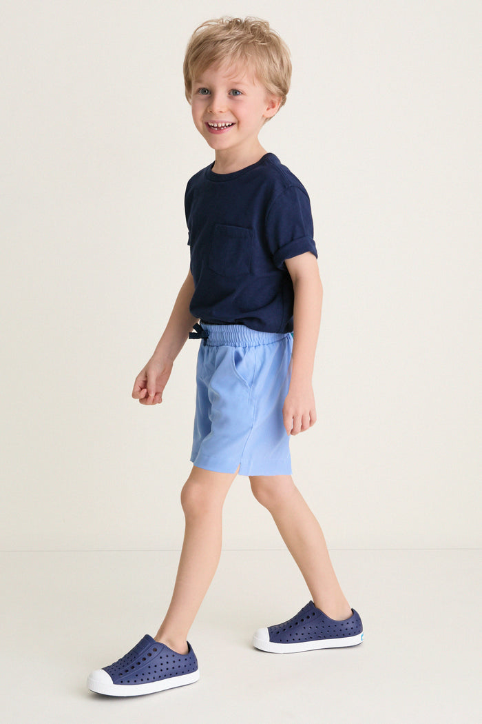 Young boy wearing Sardinia Sky Le Club Short and navy sneakers, mid-step, embodying a classic, effortless style; perfect for high-end, fun everyday wear.