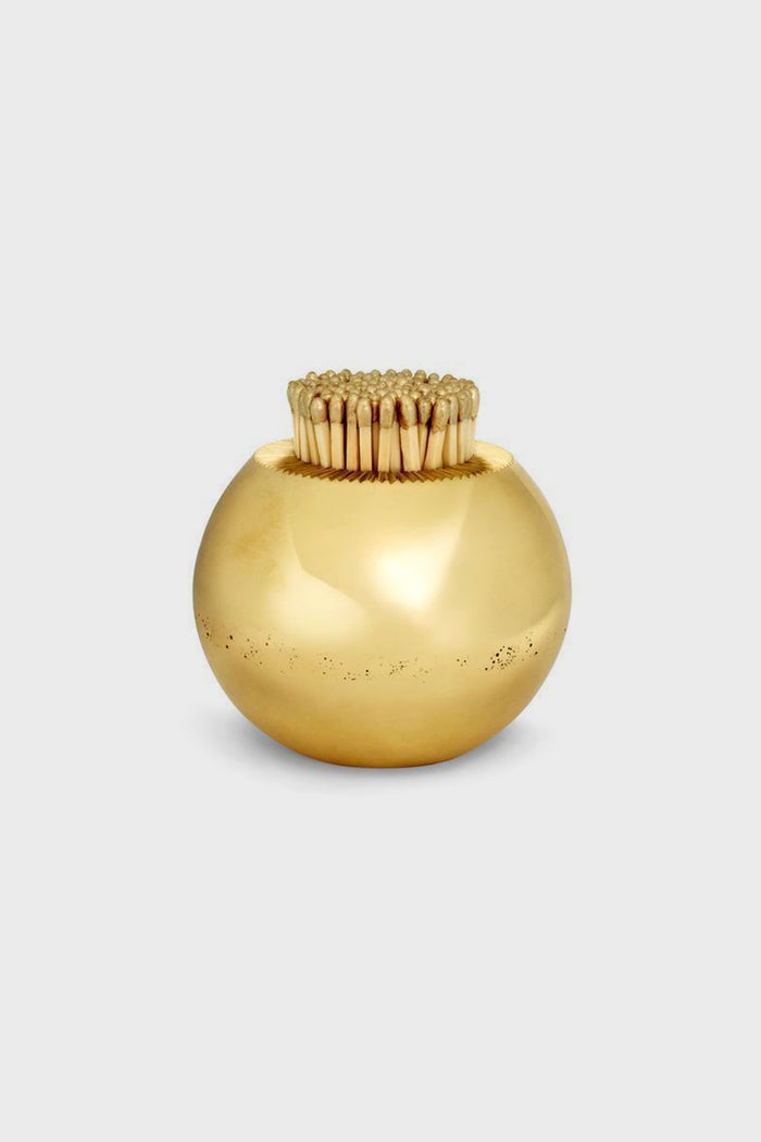 AERIN’s round, shiny gold container, crafted from solid brass as a match striker, holds upright wooden toothpicks—an elegant piece perfect for artisanal home decor.