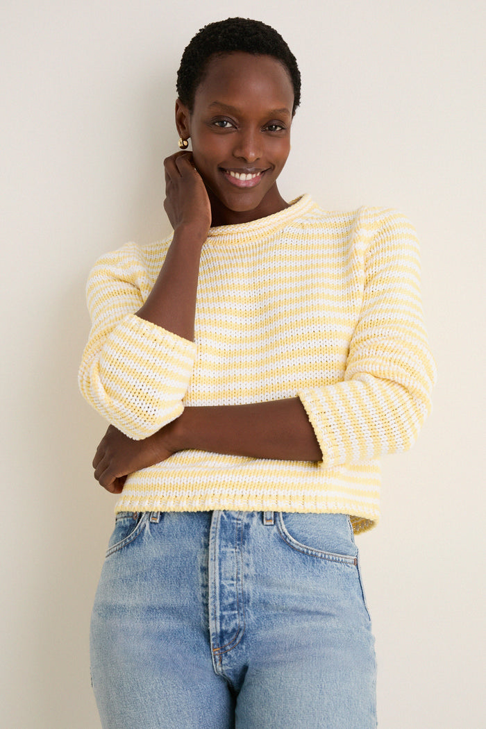 Woman in a Sunshine and Cream Fine Stripe Mini Marina Sweater, showcasing a classic, effortless style with its cozy roll-neck and slim sleeves, embodying fun, high-end fashion.